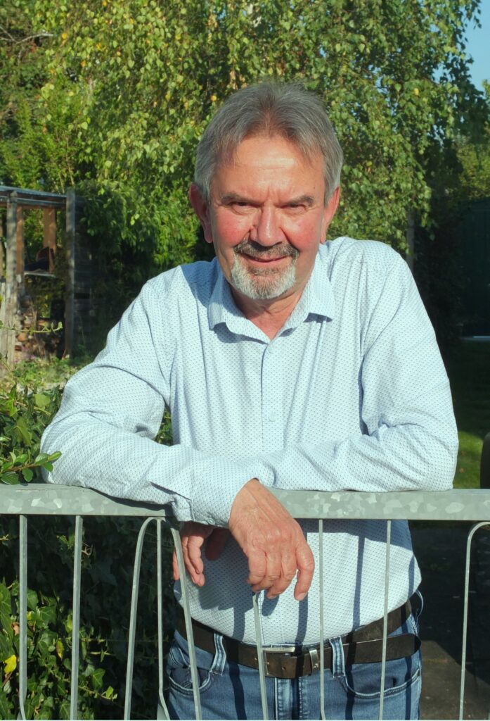 Älterer Mann lächelt im Freien am Zaun.