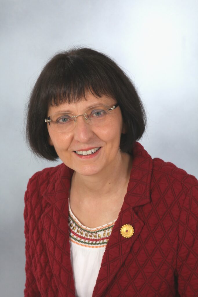 Frau mit rotem Blazer und Brille lächelnd.