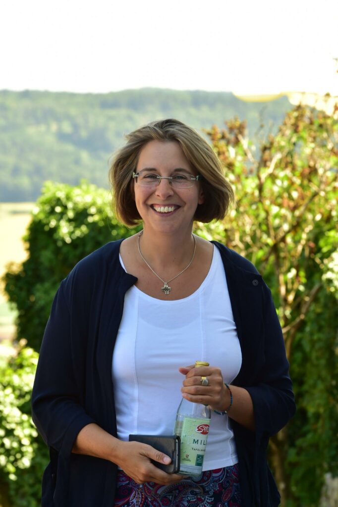 Frau in der Natur lächelt mit Getränkflasche.