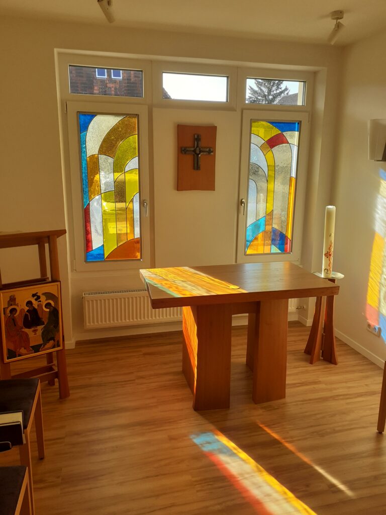 Kleiner Raum mit bunten Glasfenstern und Tisch.