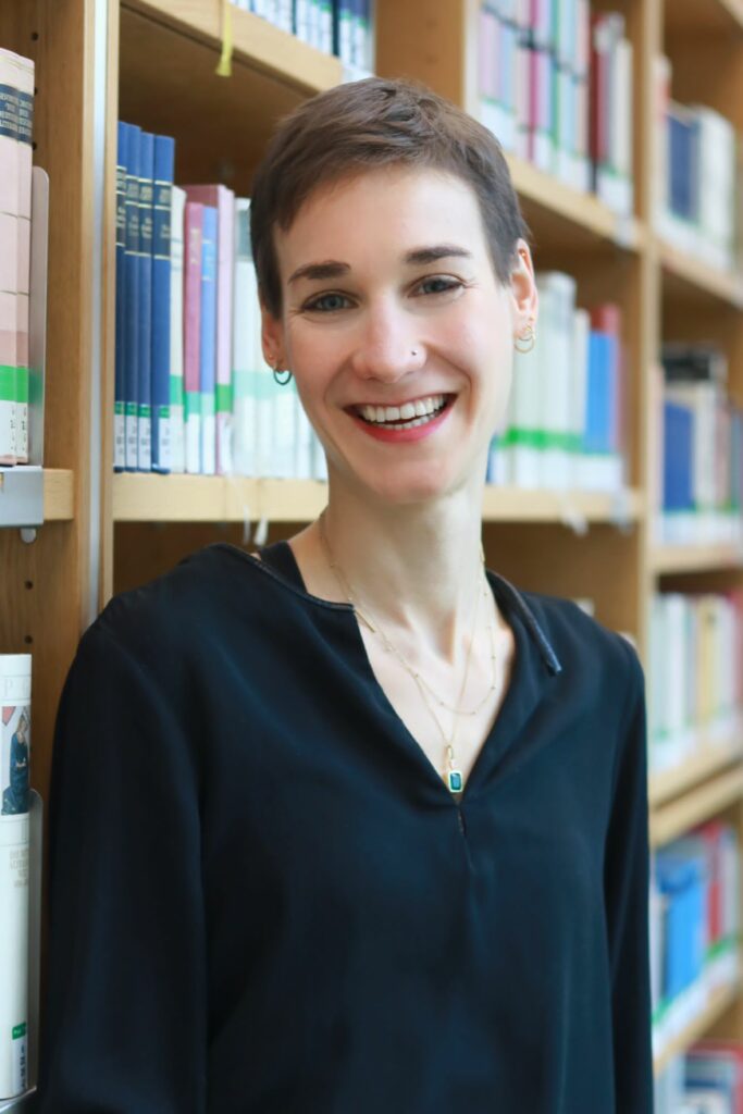 Eine lächelnde Frau in einer Bibliothek stehend.