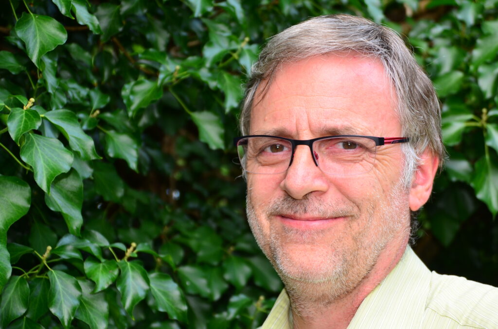 Mann mit Brille vor grünen Blättern lächelnd