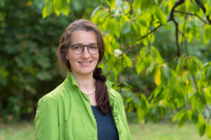 Frau im Grünen vor einem Baum stehend