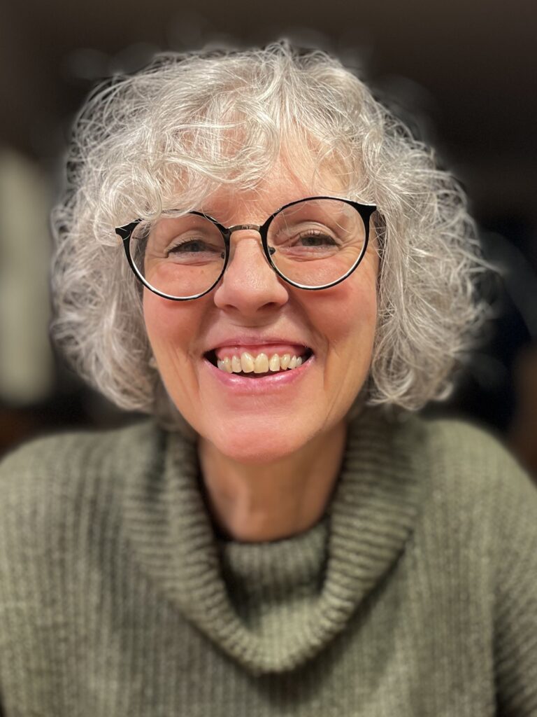 Lächelnde Frau mit Brille und lockigem Haar.