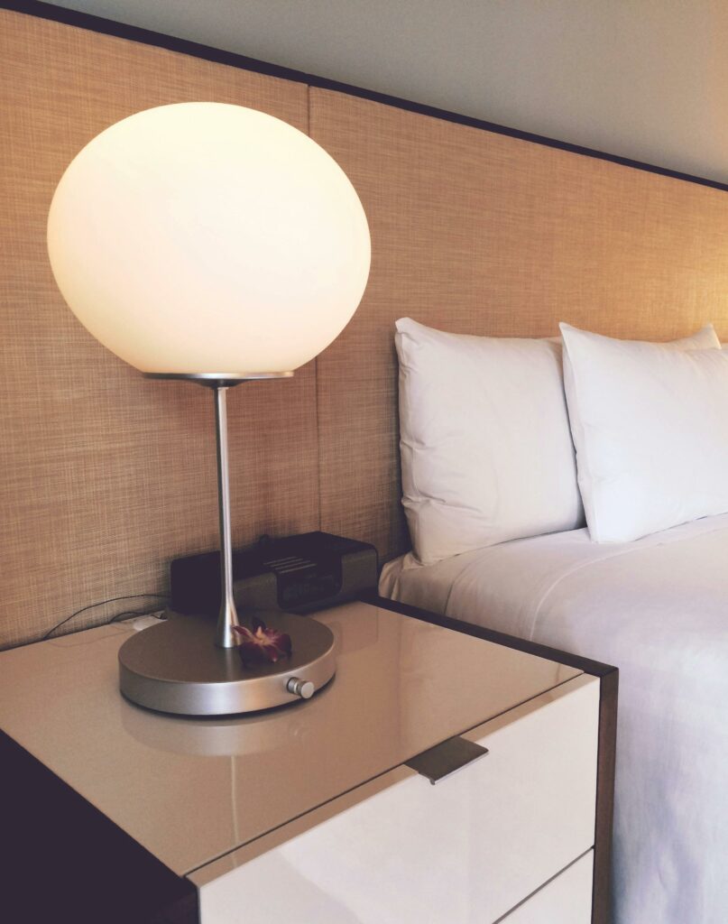 Nachttischlampe neben gemütlichem weißen Bett im Zimmer