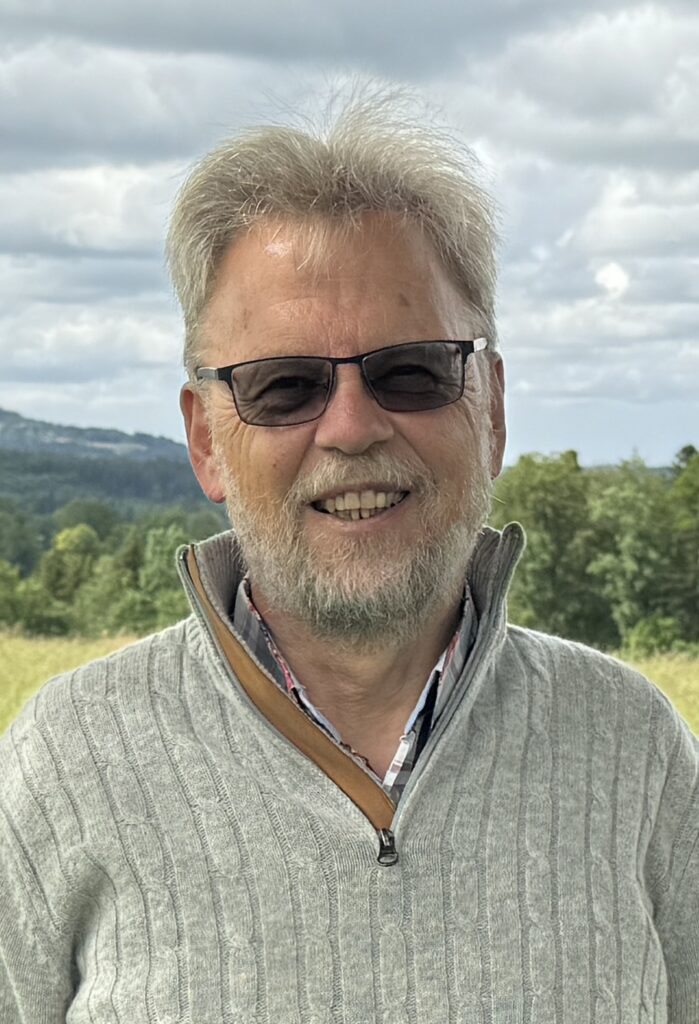 Mann mit Brille lächelt in die Kamera draußen.