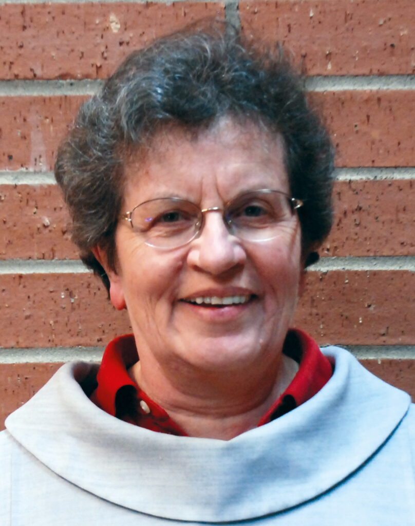 Ältere Frau mit Brille vor Ziegelwand lächelnd