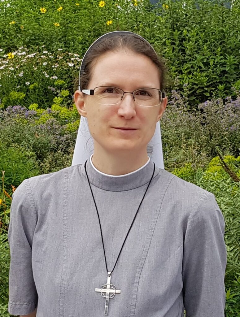 Frau in Nonnentracht steht im blühenden Garten.