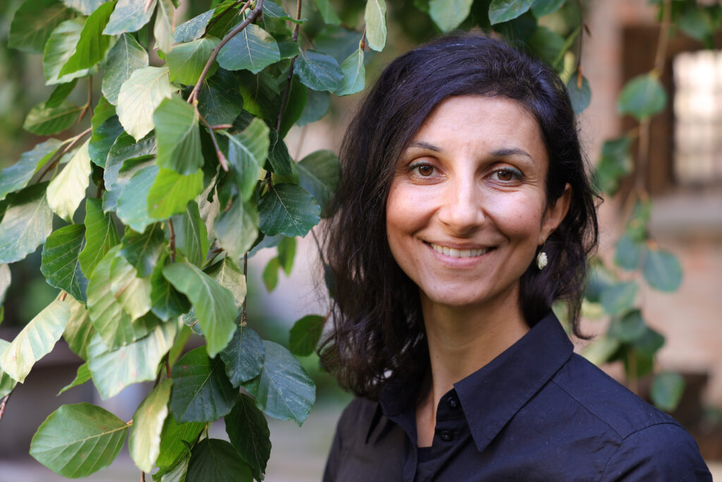 Eine Frau lächelt vor grünen Blättern draußen